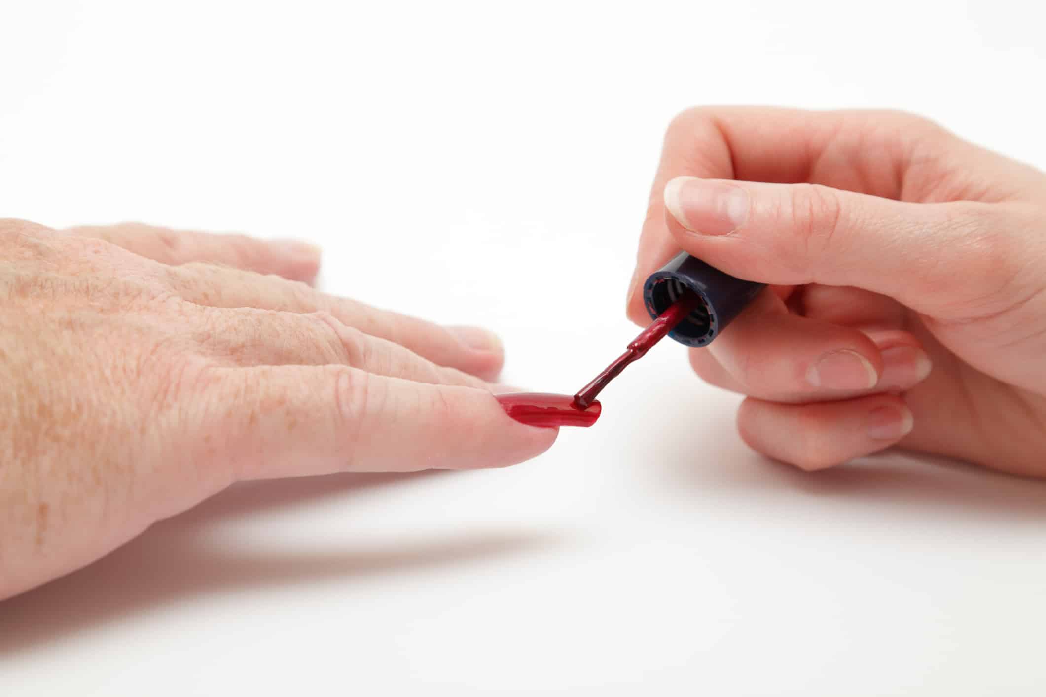 female hand paints nail polish on male long nail against a plain background (not isolated)