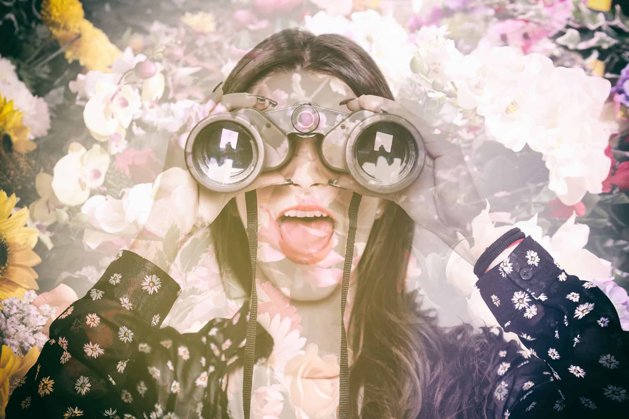 Double exposure of surprised girl looking through binoculars and flowers