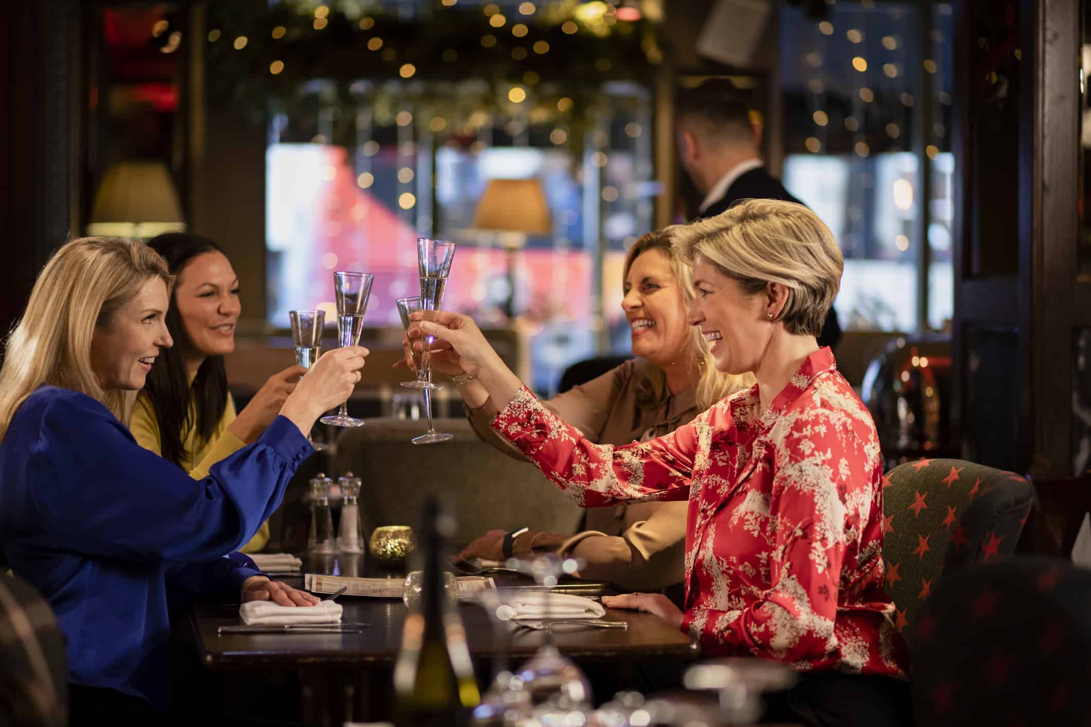 Small group of mature female friends making a celebratory toast while sitting around a table in a restaurant.