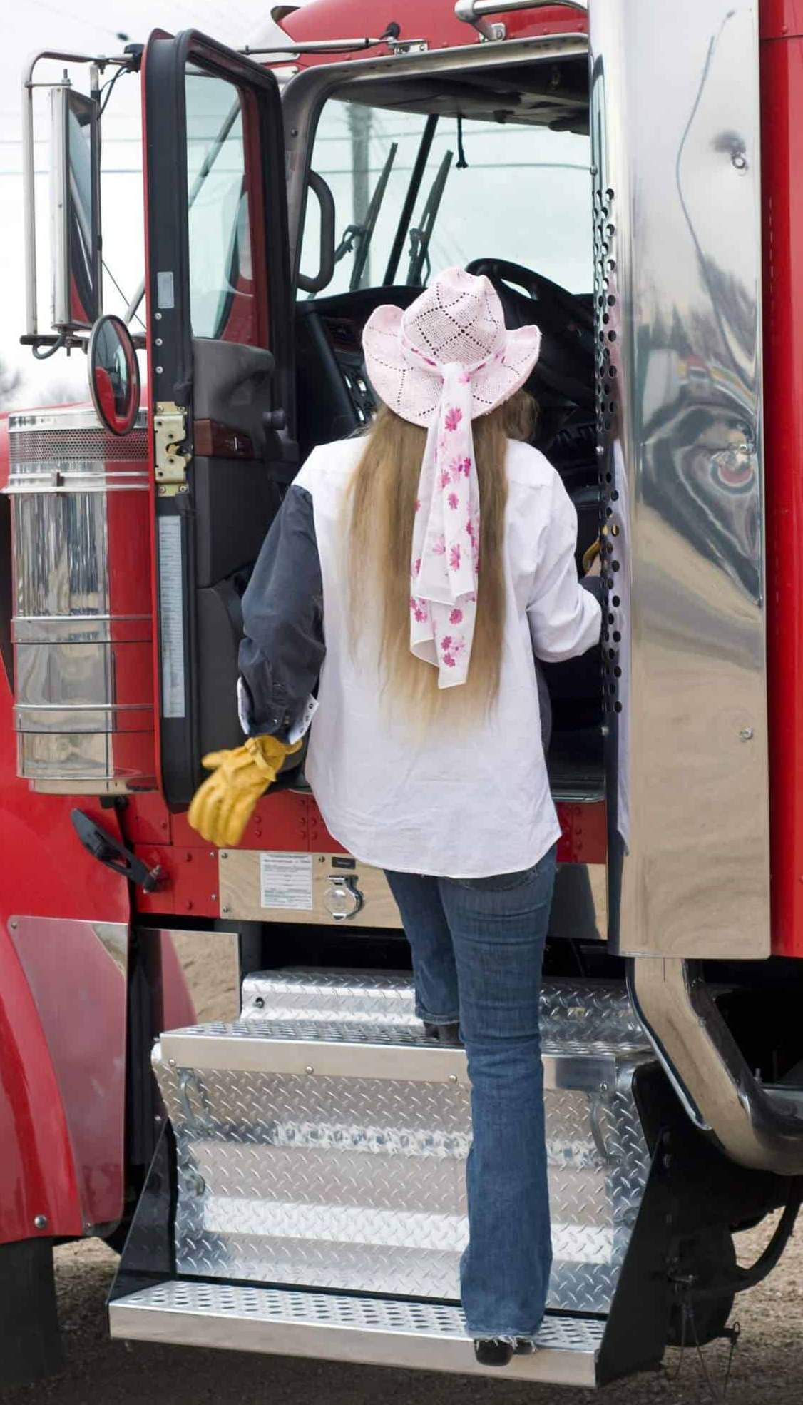 A woman truck driver enters the cab of a big rig.