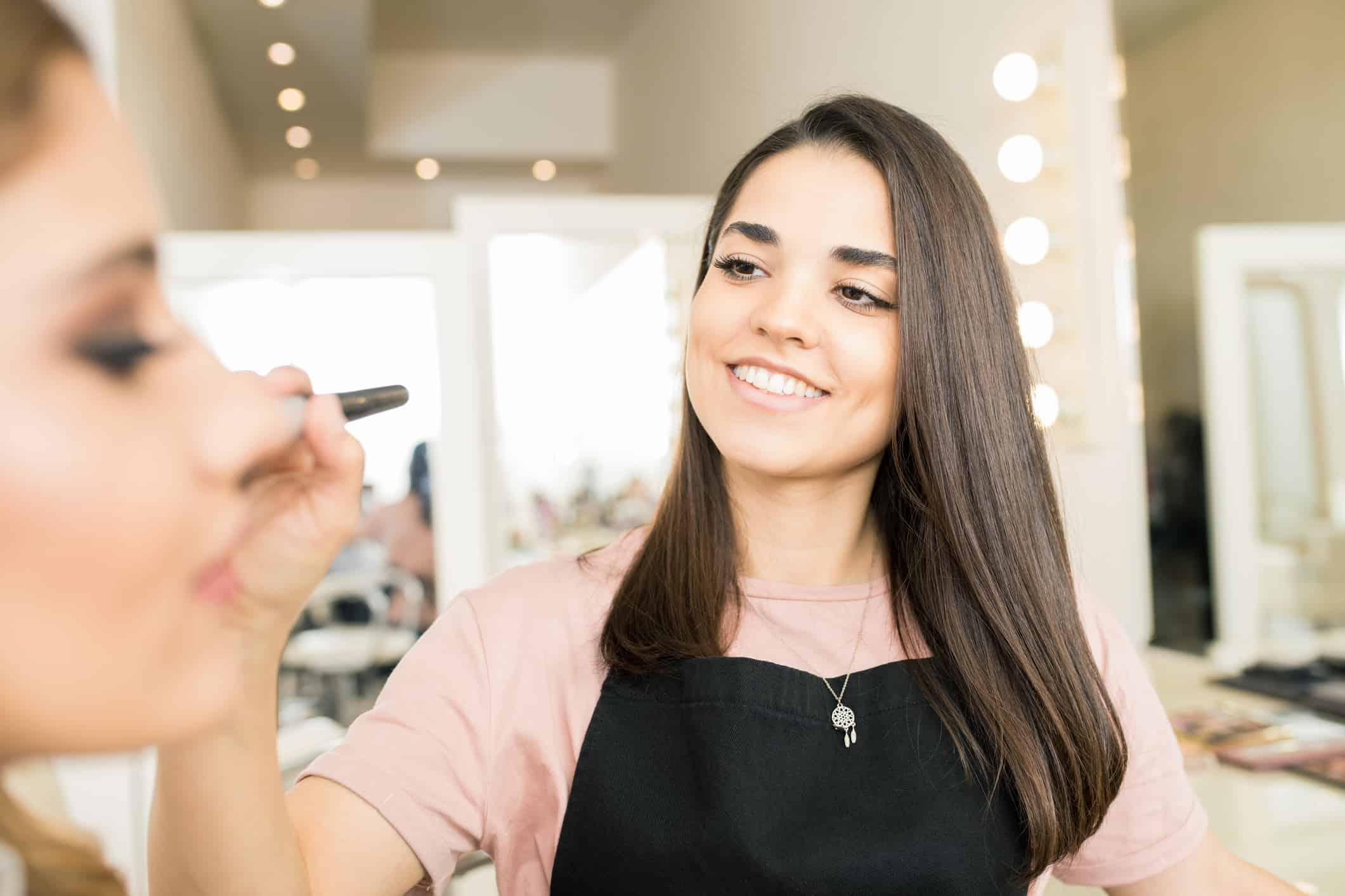 Portrait of a cute Hispanic make-up artist doing her job with a customer in a beauty salon